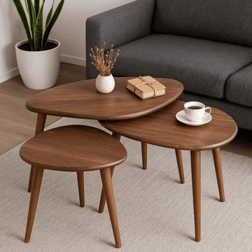 Three nested oval nesting coffee tables in a warm medium brown wood finish, styled in a living room setting with a gray sofa, a potted plant, and tabletop decor.